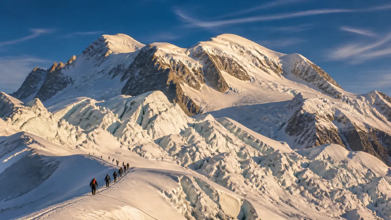 Seilschaft im Aufstieg über einen Gletscherkamm vor dem Mont-Blanc-Massiv im Abendlicht
